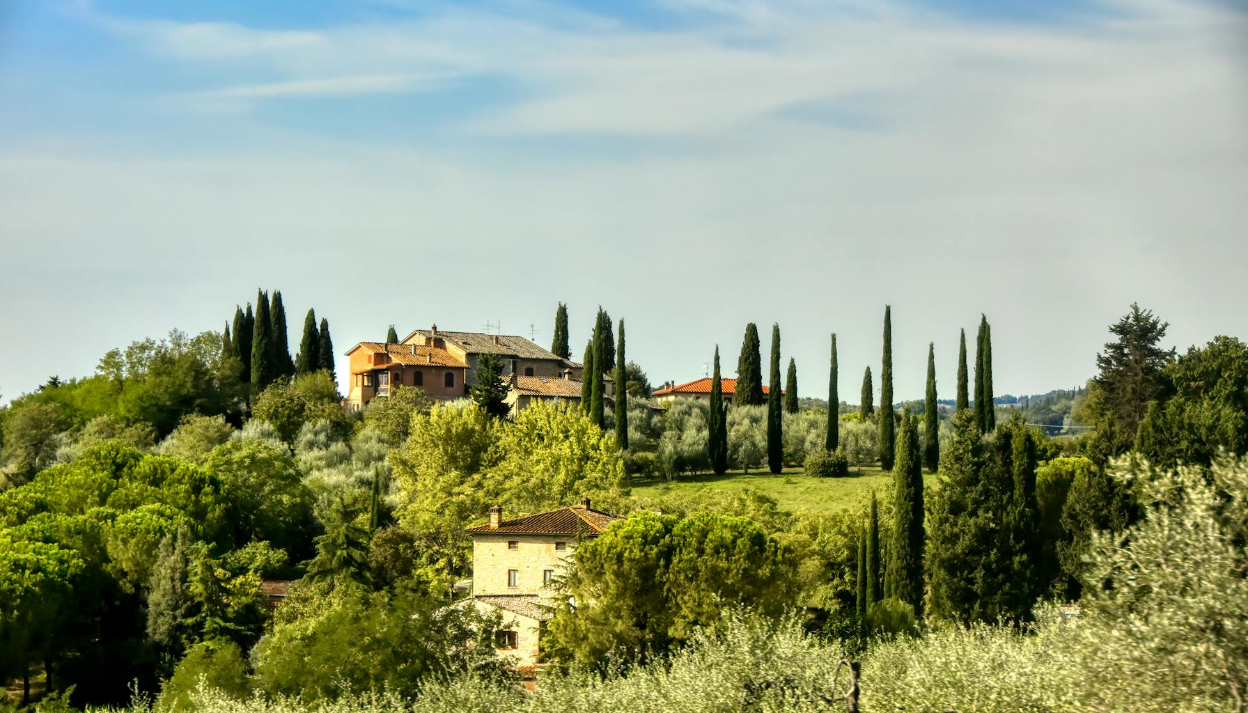 Charming view of Tuscan countryside with traditional villas and lush greenery under a clear sky. — Foto: Marc Peeters (Pexels)